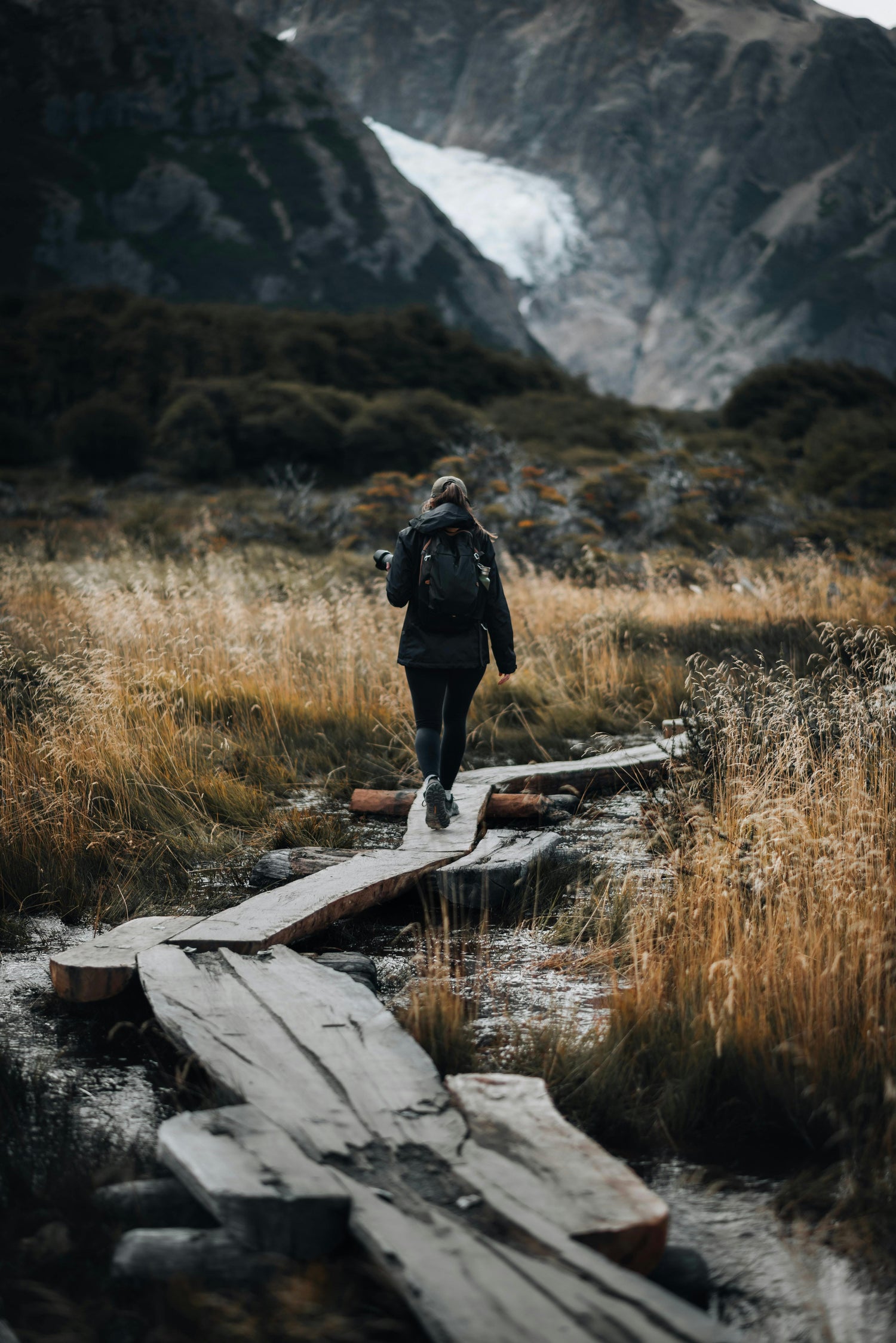 Person walking on a wooden path in a mountainous landscape with a glacier in the background